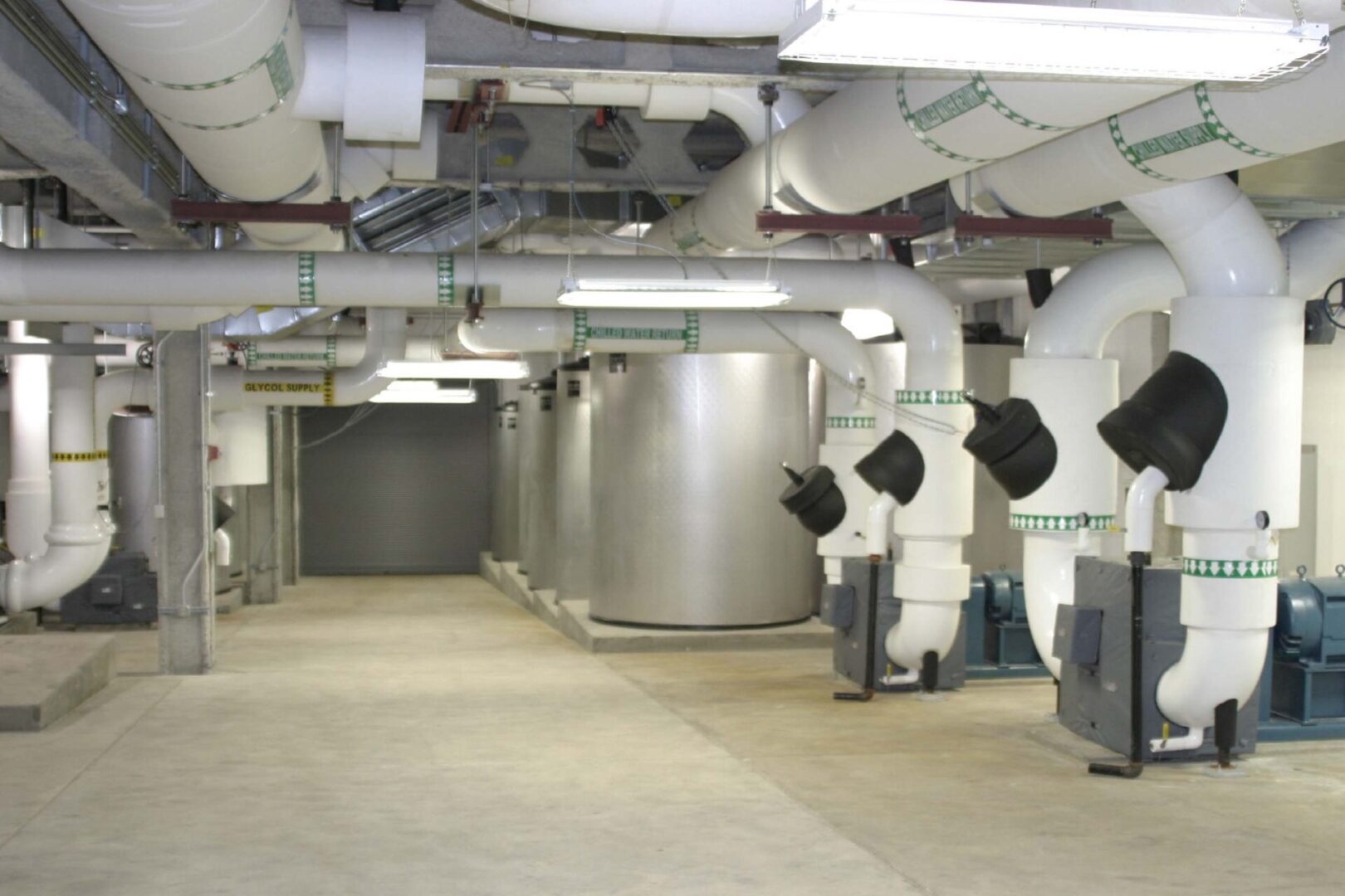 Industrial room with large metallic tanks and ventilation pipes.