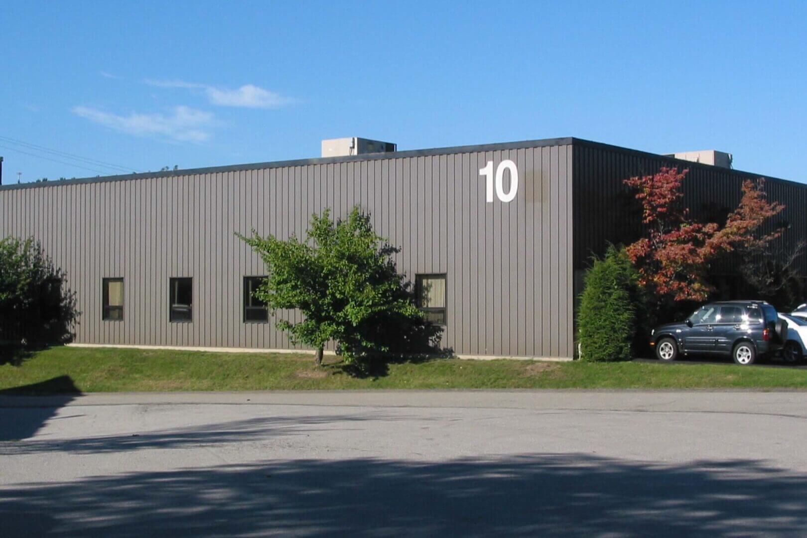 A gray industrial building with the number 10 on the upper corner, surrounded by trees.