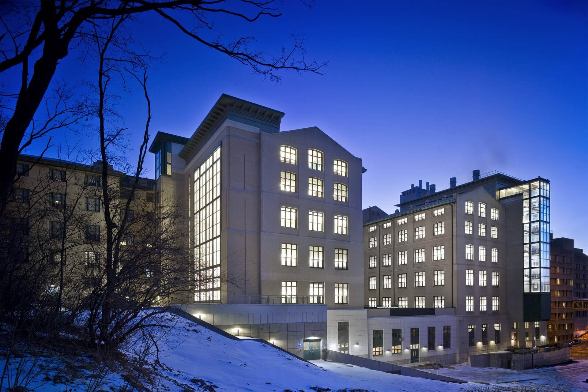 Modern buildings illuminated at dusk in a snowy landscape.