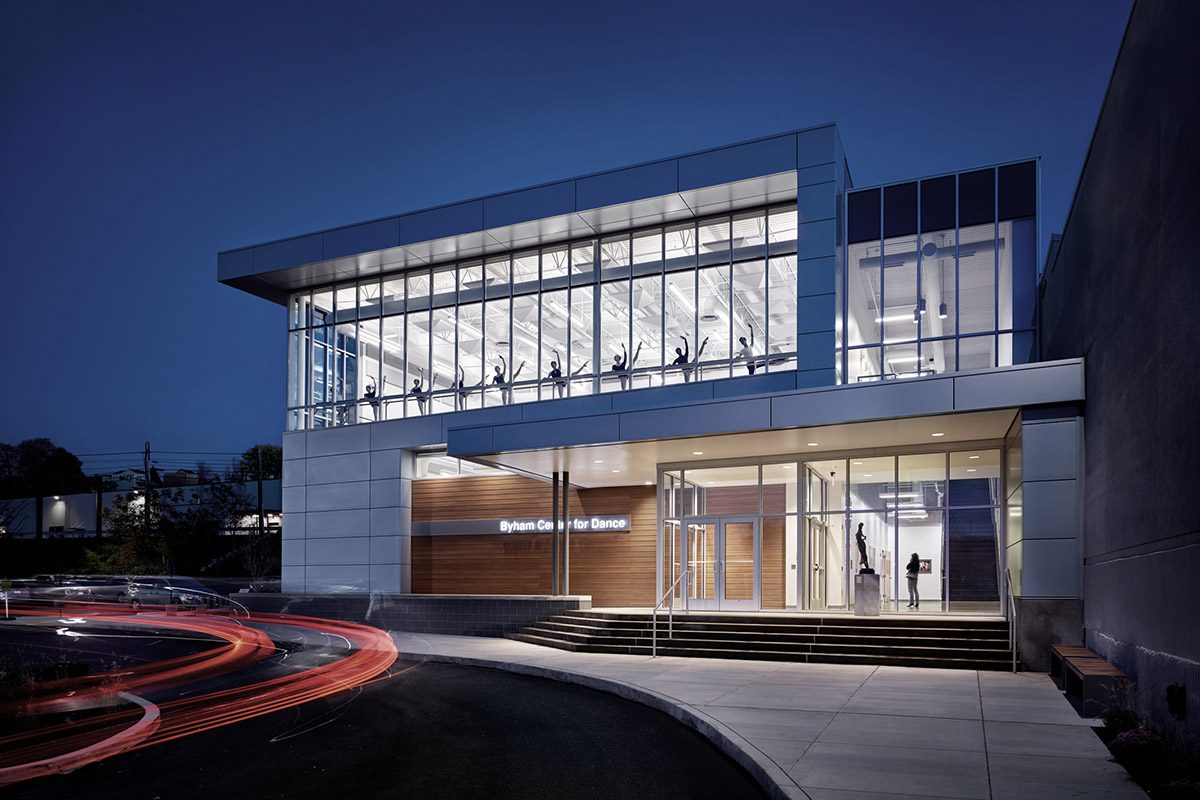 Modern glass building illuminated at night with car light trails.