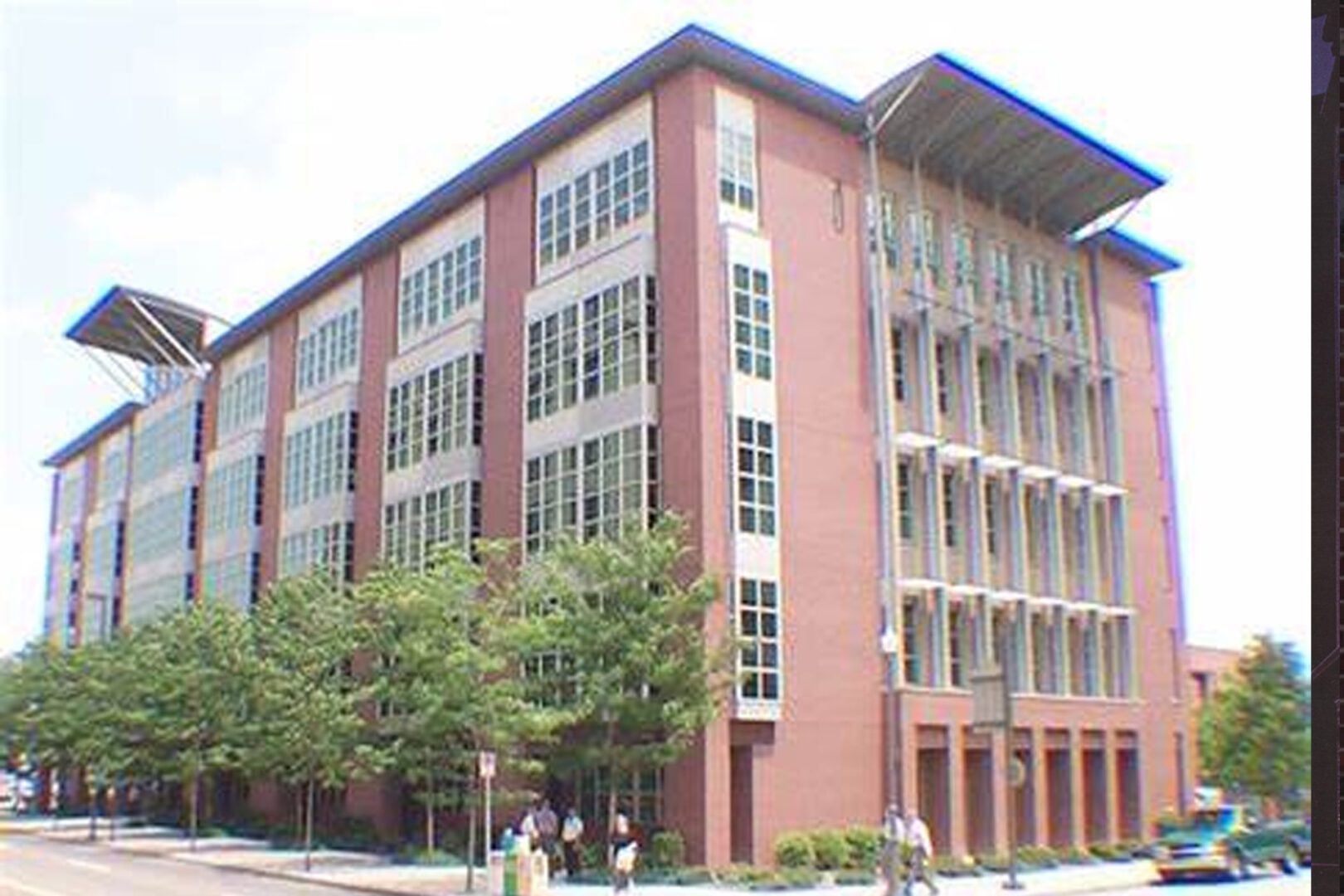 A large brick building with many windows and trees in front.