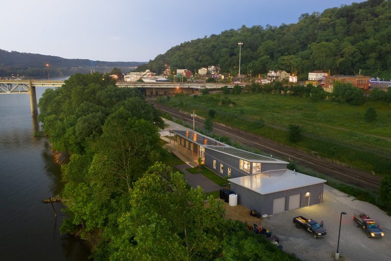 Riverside building with surrounding greenery and bridge.