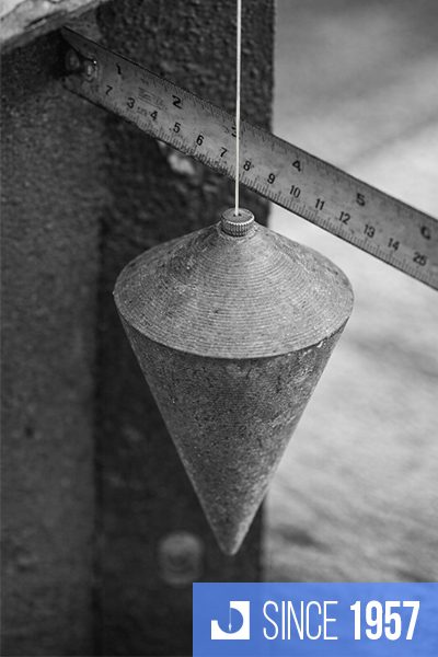 Conical metal plumb bob suspended next to ruler